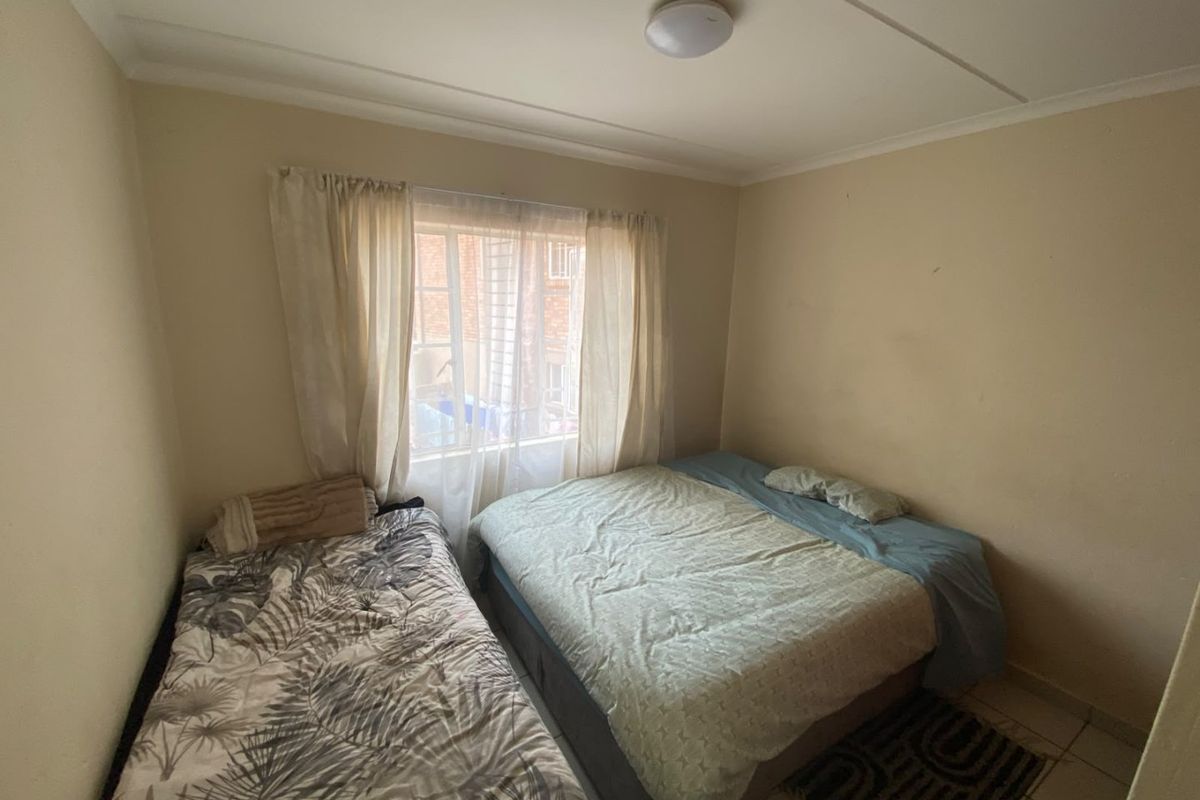 A compact bedroom featuring tiled flooring and a window with security bars, requiring minor cosmetic updates to improve its overall appeal.