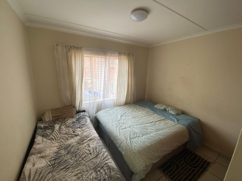 A compact bedroom featuring tiled flooring and a window with security bars, requiring minor cosmetic updates to improve its overall appeal.