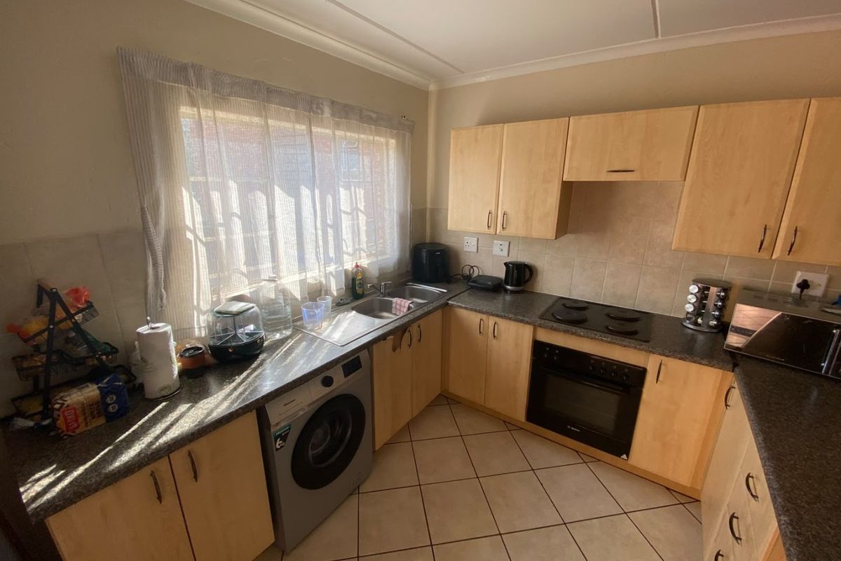 Functional kitchen featuring light wood cabinetry, granite countertops, built-in oven, electric hob, and tiled flooring with ample natural light.