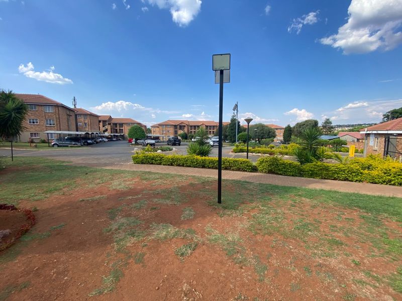 Exterior view of the apartment complex grounds featuring paved driveways, covered parking bays, and landscaped garden areas under a clear sky.