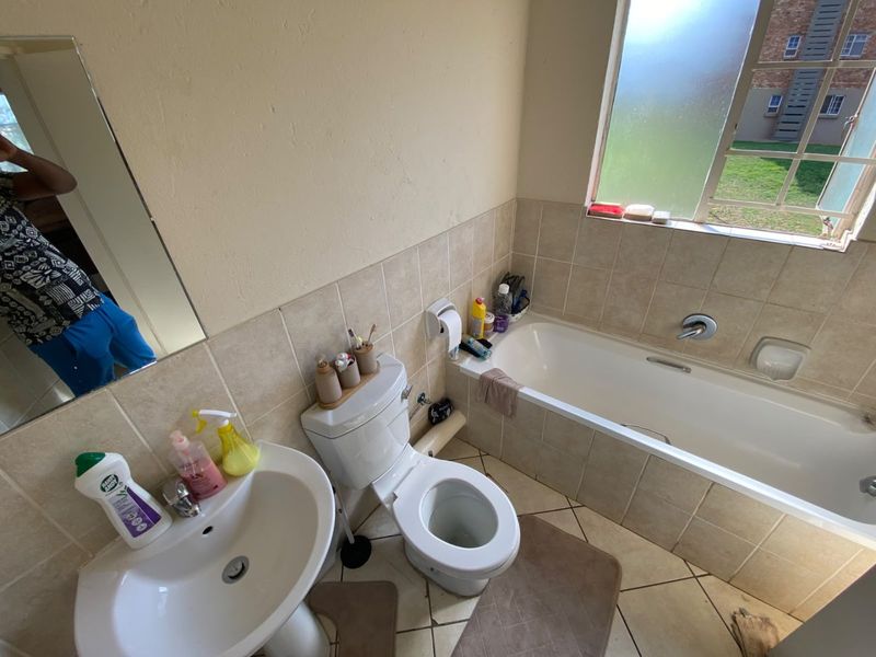 A functional bathroom featuring a pedestal basin, toilet, and bathtub with tiled splashbacks and flooring, offering a practical layout with natural light.
