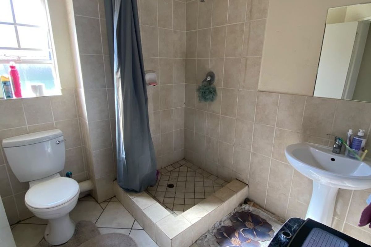 A functional bathroom featuring a pedestal basin, toilet, and a tiled shower cubicle. The space shows signs of ceiling water damage and dated finishes.
