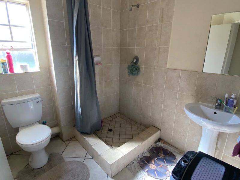 A functional bathroom featuring a pedestal basin, toilet, and a tiled shower cubicle. The space shows signs of ceiling water damage and dated finishes.