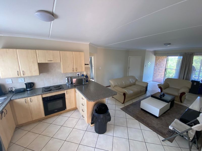 Open-plan living area featuring a functional kitchen with built-in cabinetry, electric hob, and oven, flowing into a lounge space with access to a balcony.