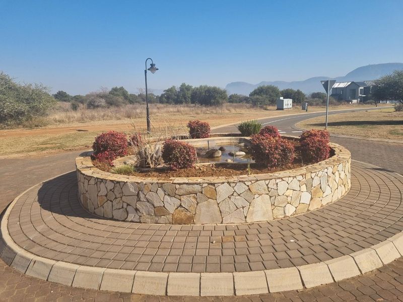 A well-maintained circular stone-clad planter and water feature located in the center of a paved roundabout within a residential estate.