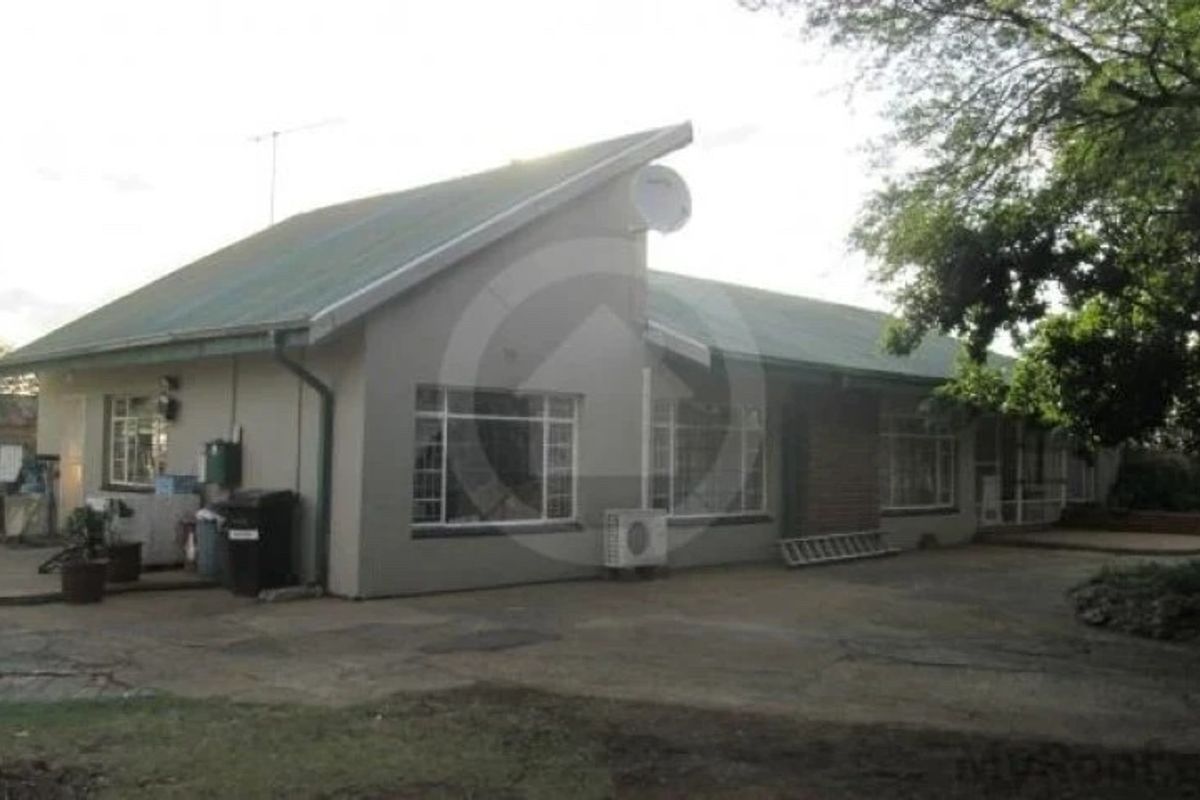 Rear view of a commercial building featuring a pitched metal roof, brick chimney, and paved outdoor area with an installed air conditioning unit.