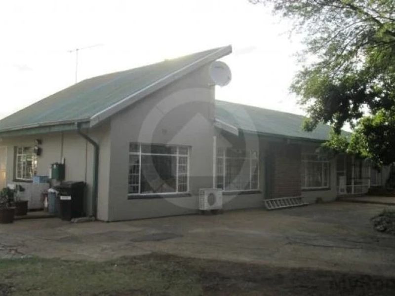 Rear view of a commercial building featuring a pitched metal roof, brick chimney, and paved outdoor area with an installed air conditioning unit.