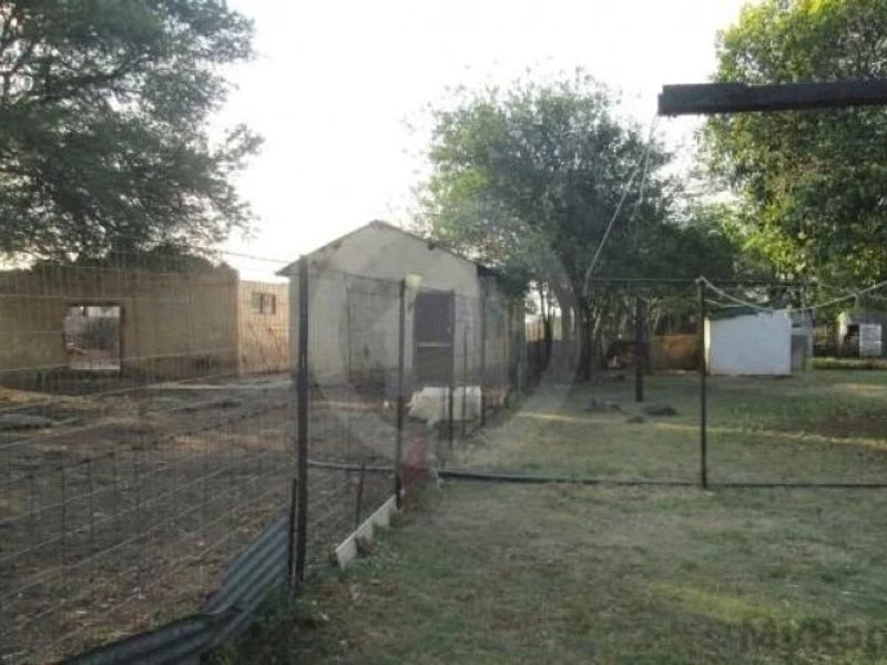Rear exterior view of the property featuring multiple outbuildings, wire fencing, and mature trees on a large plot of land.