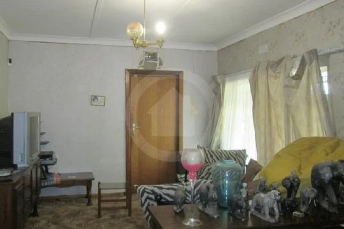 A dated living room featuring traditional coving, a timber door, and large windows, offering potential for modernization and cosmetic updates.