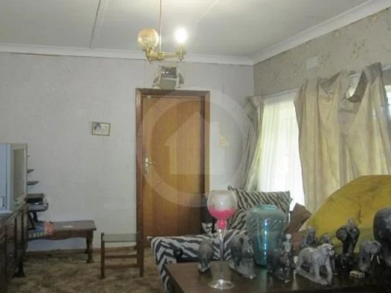 A dated living room featuring traditional coving, a timber door, and large windows, offering potential for modernization and cosmetic updates.