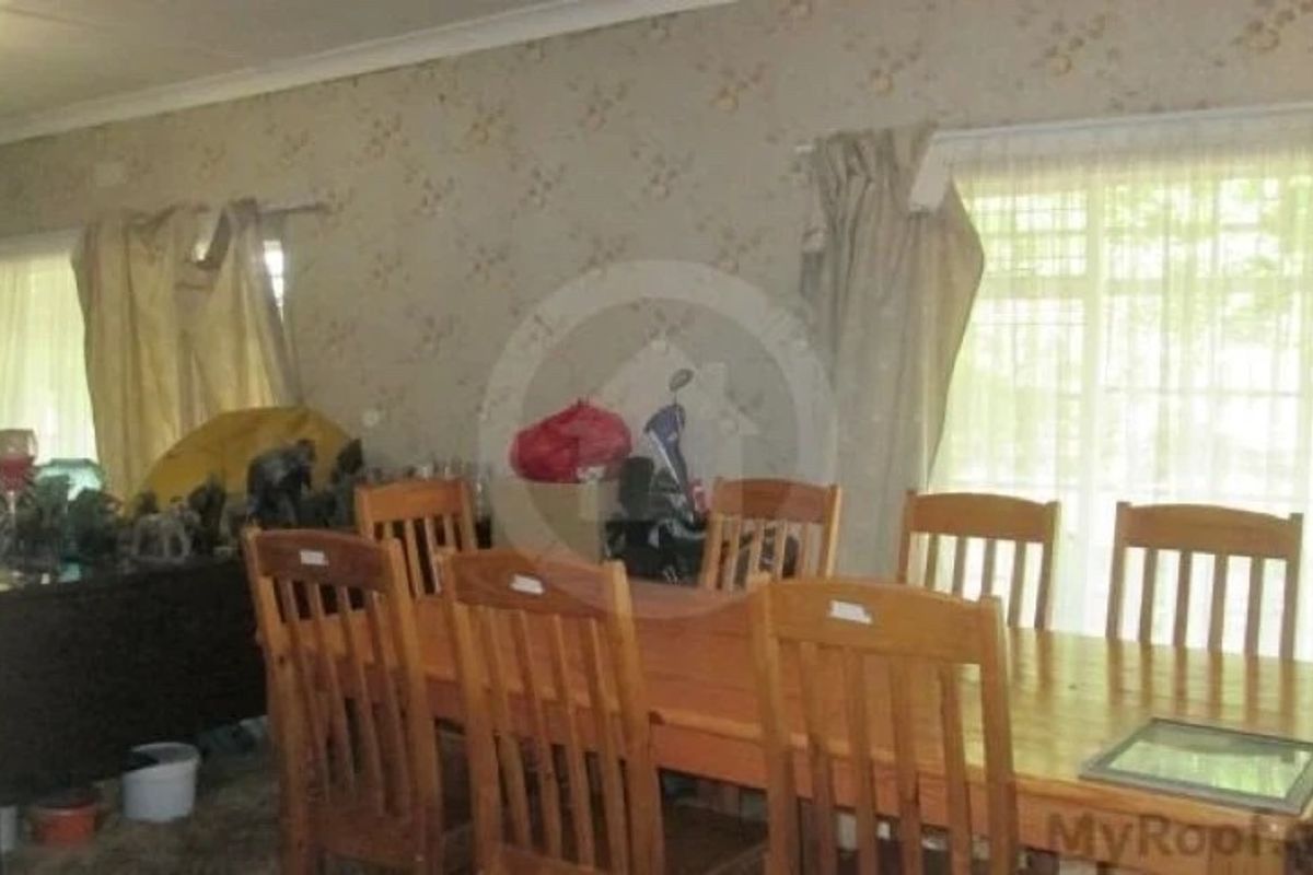 A dining room featuring large windows and dated wallpaper, offering a functional space that would benefit from modern cosmetic updates.
