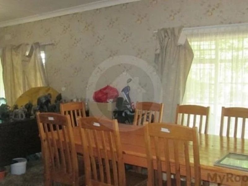 A dining room featuring large windows and dated wallpaper, offering a functional space that would benefit from modern cosmetic updates.