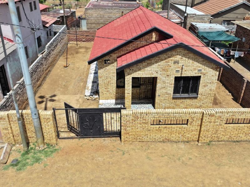 Aerial view of a face brick house with a red tiled roof, featuring a perimeter wall and secure gated entrance.