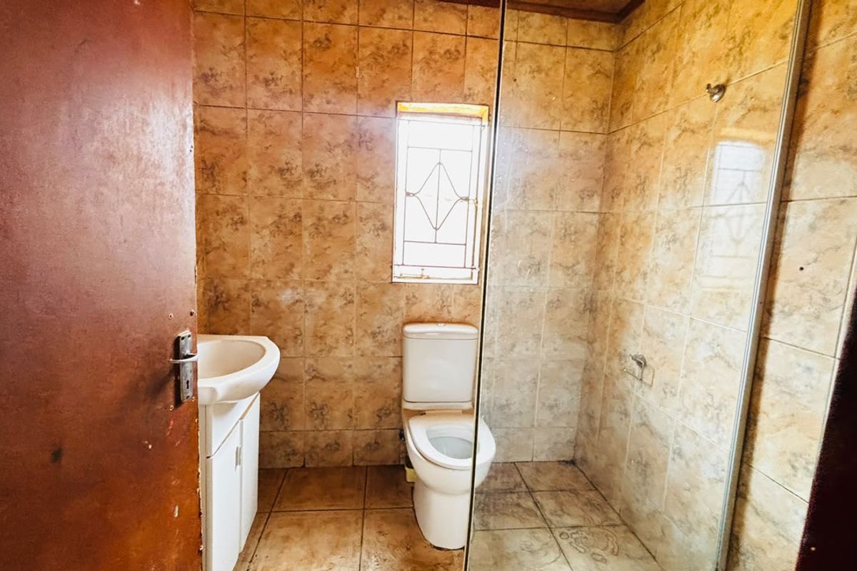 A functional bathroom featuring a pedestal basin, toilet, and glass-enclosed shower, finished with dated ceramic wall and floor tiles.
