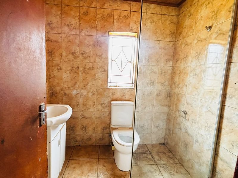 A functional bathroom featuring a pedestal basin, toilet, and glass-enclosed shower, finished with dated ceramic wall and floor tiles.