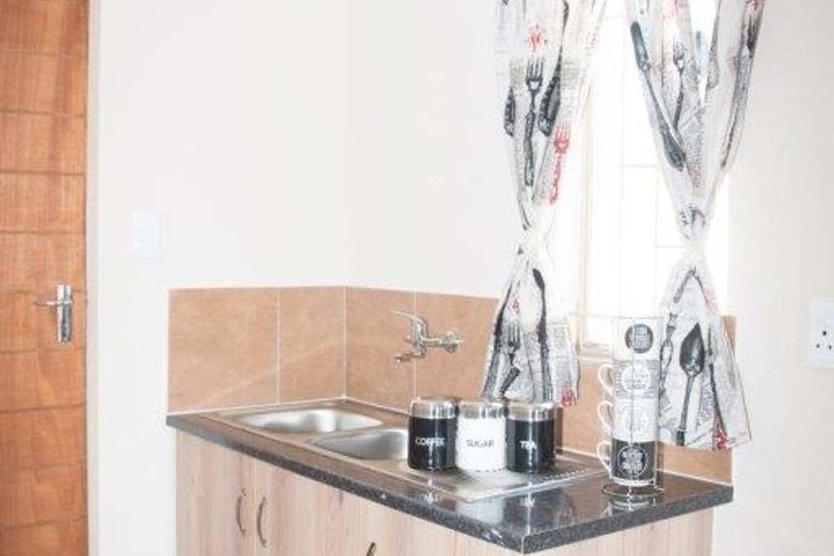 A compact kitchen area featuring wood-look cabinetry, a stainless steel sink, tiled splashback, and tiled flooring.