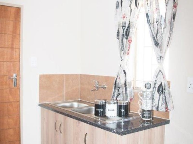 A compact kitchen area featuring wood-look cabinetry, a stainless steel sink, tiled splashback, and tiled flooring.