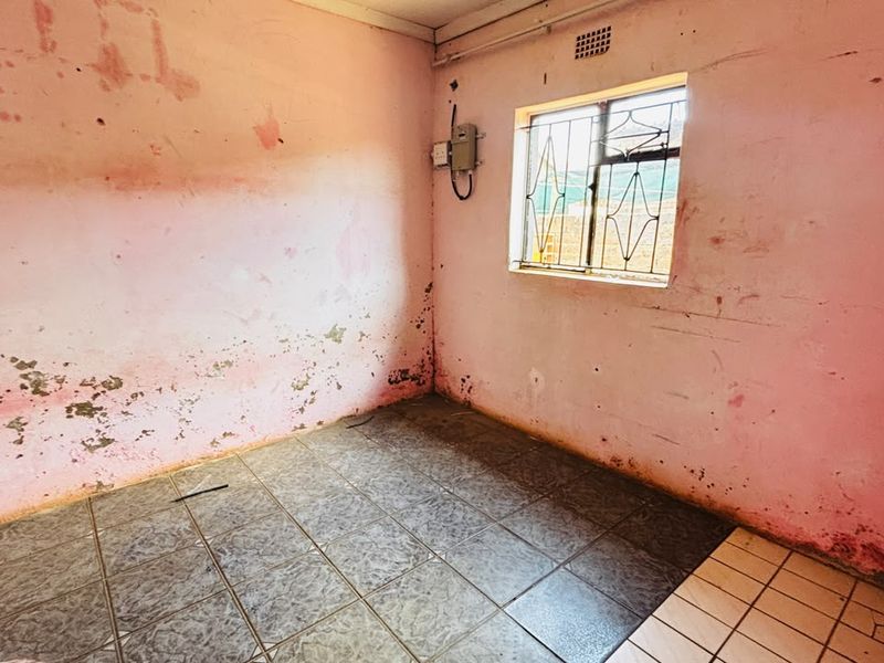 An empty bedroom featuring tiled flooring and security bars on the window, requiring significant wall surface repairs and repainting.
