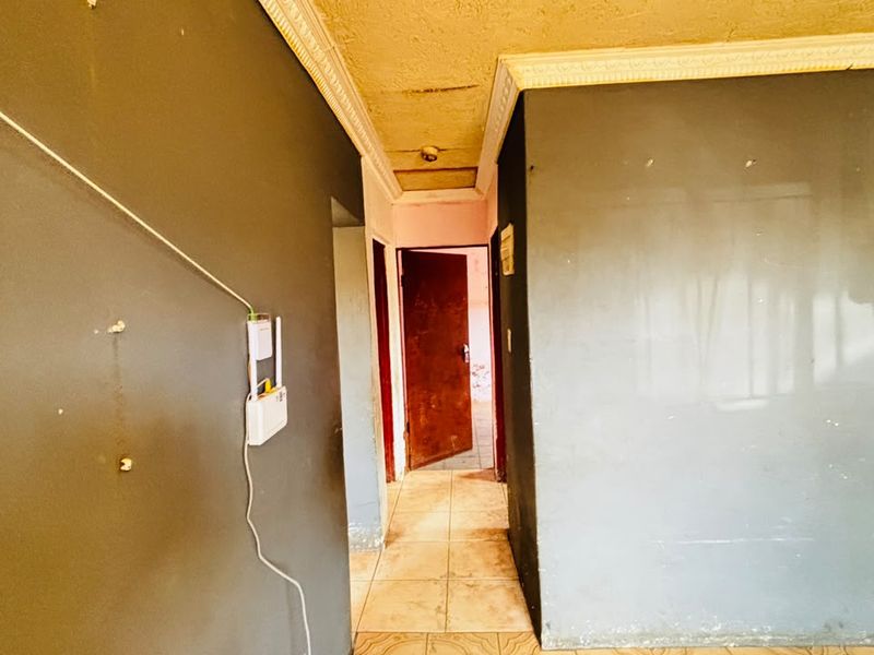 A narrow hallway featuring tiled flooring and crown molding, currently in need of cosmetic repairs and fresh paint to restore its condition.