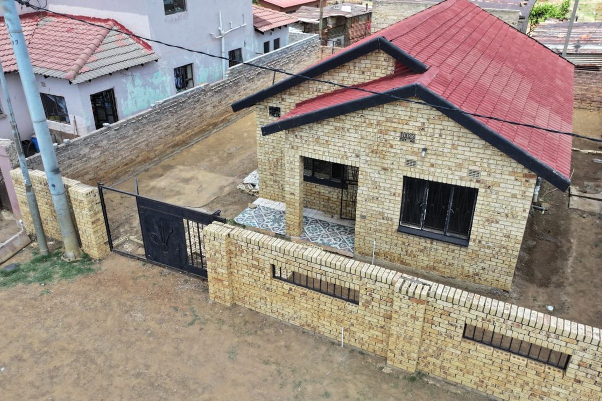 Aerial view of a face brick house featuring a red tiled roof, perimeter wall with metal gate, and a tiled entrance porch.