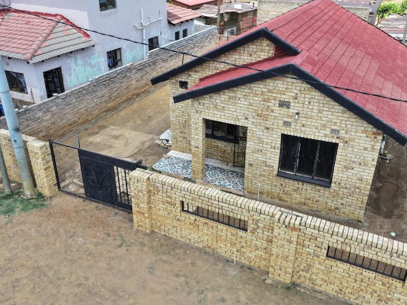 Aerial view of a face brick house featuring a red tiled roof, perimeter wall with metal gate, and a tiled entrance porch.