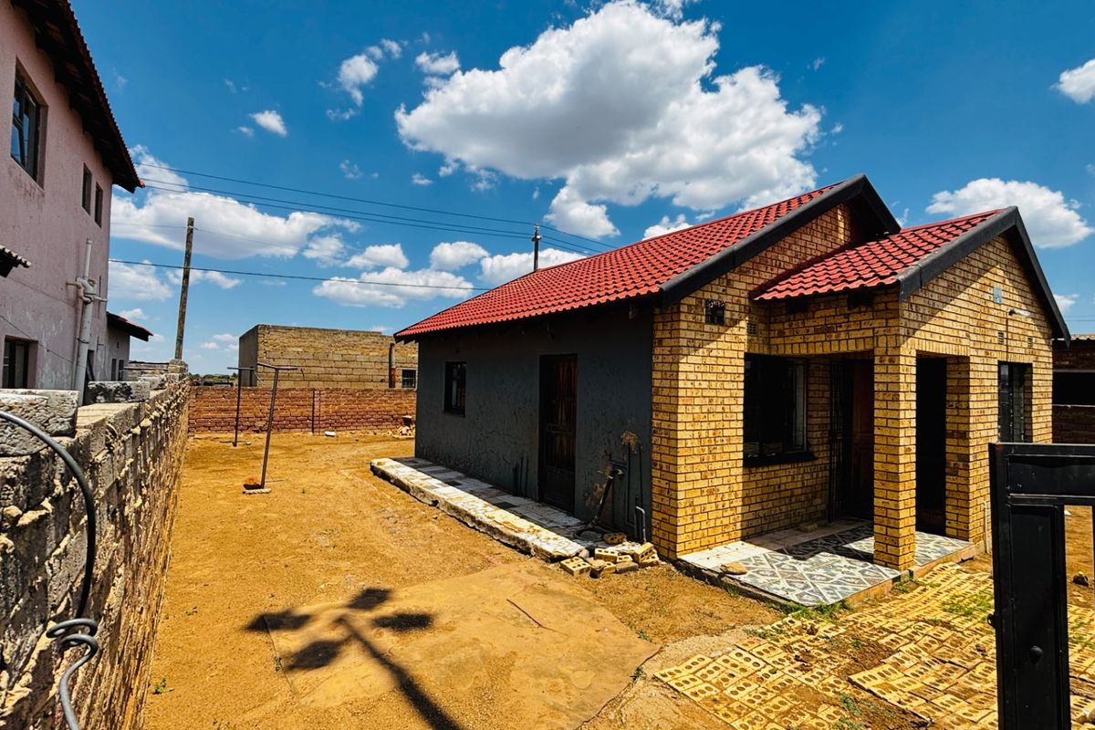 Front view of a face brick house featuring a red tiled roof and a covered entrance porch, set on a plot with paved areas.