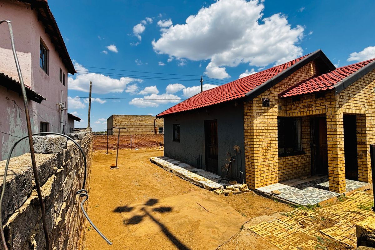 Rear view of a face brick house with a tiled roof, featuring an unlandscaped yard and boundary wall.