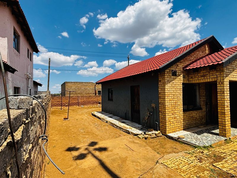 Rear view of a face brick house with a tiled roof, featuring an unlandscaped yard and boundary wall.