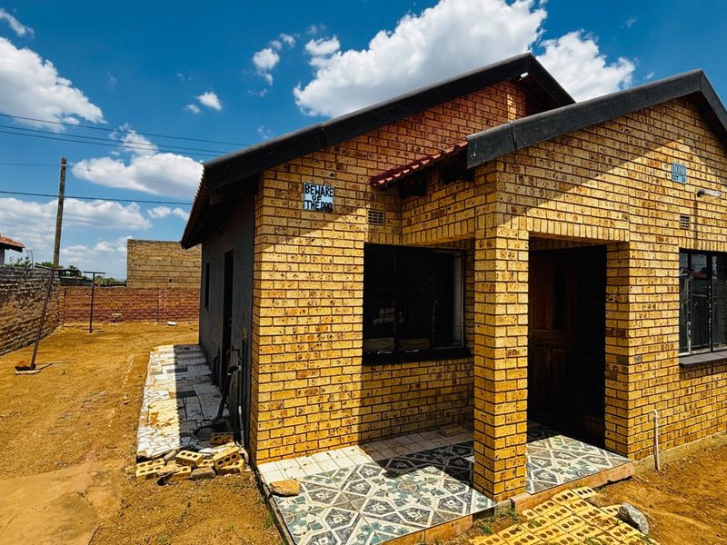 A single-story face brick house featuring a covered entrance porch, metal window frames, and an expansive, undeveloped yard area.