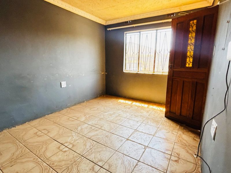 An empty bedroom featuring tiled flooring, a timber door, and security bars on the window, with dark grey painted walls.