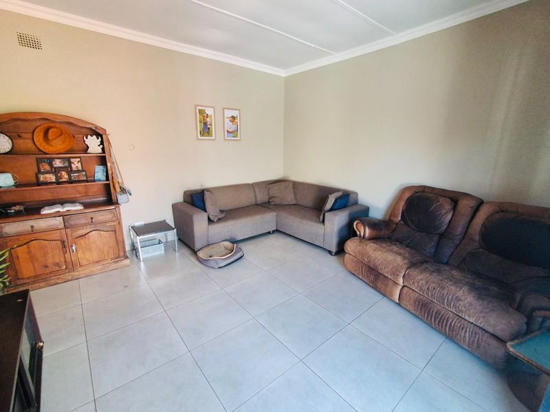 A spacious living room featuring neutral wall tones, large format floor tiles, and classic ceiling cornicing, providing a versatile base for interior updates.