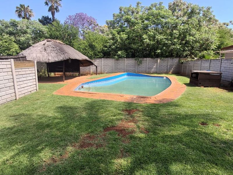 Outdoor pool area featuring a swimming pool, paved surround, and a traditional thatch lapa, enclosed by a brick boundary wall.