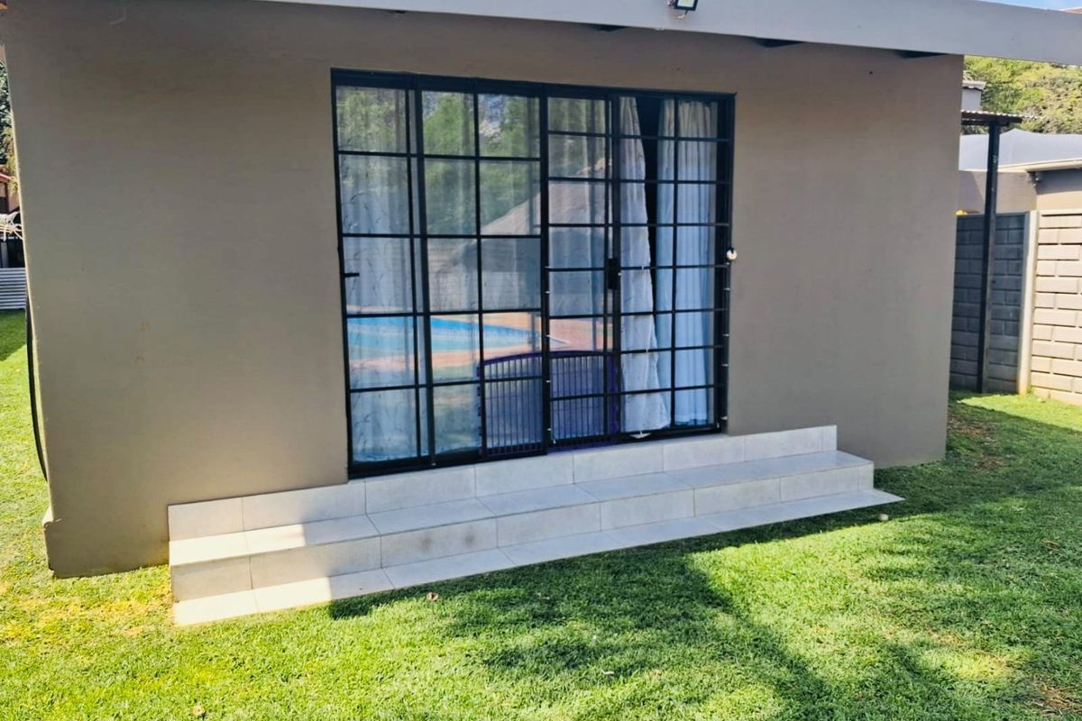 Rear exterior view of the townhouse featuring tiled patio steps leading to black framed sliding glass doors with integrated security gate.