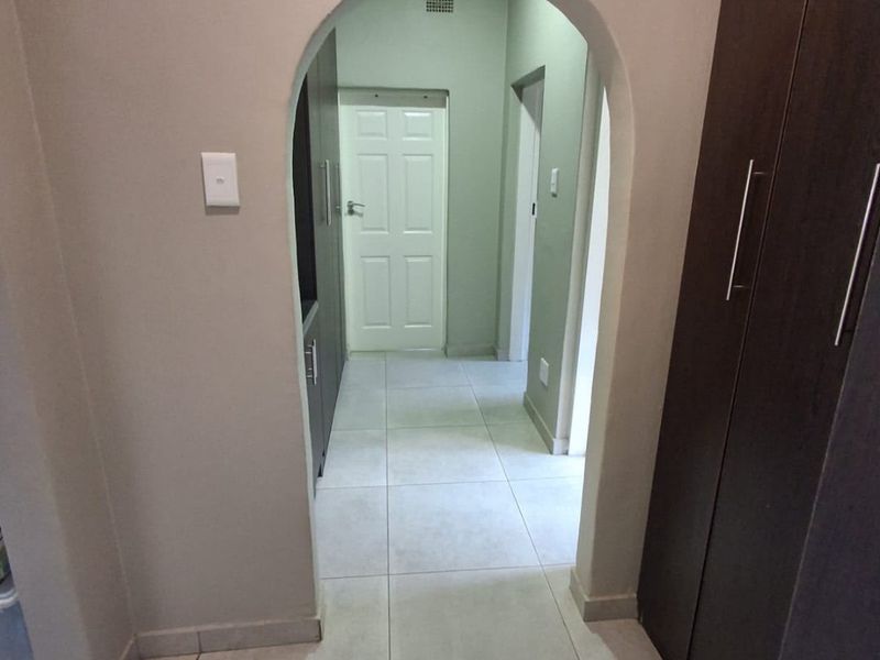 A clean, neutral hallway featuring an arched entryway, tiled flooring, and built-in storage cupboards leading to interior rooms.