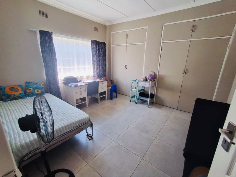 A spacious bedroom featuring neutral tiled flooring, built-in cupboards, and large windows that provide ample natural light.