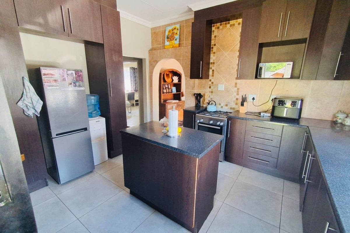 A functional kitchen featuring dark wood cabinetry, granite countertops, a central island, and a tiled backsplash with a gas stove and built-in oven.