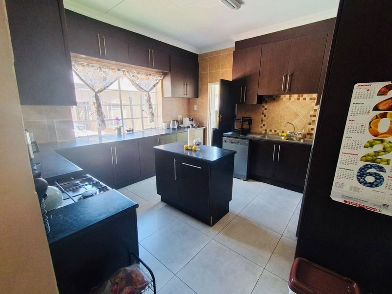 A functional kitchen featuring dark wood cabinetry, granite countertops, a central island, gas hob, and tiled flooring with a neutral backsplash.