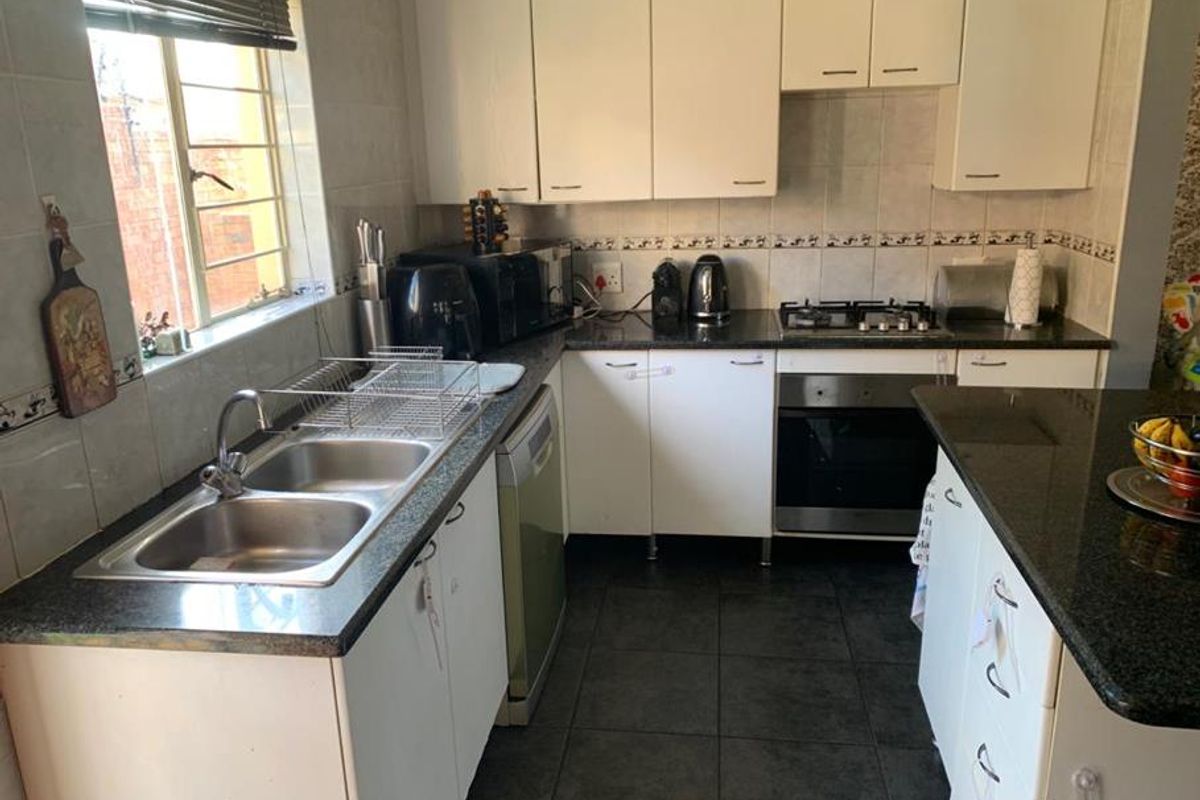 Functional kitchen featuring white cabinetry, granite countertops, a gas hob, built-in oven, and a double bowl stainless steel sink with tiled finishes.