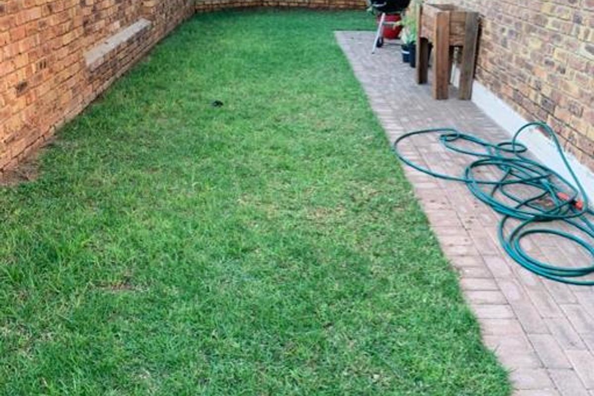 A private rear garden featuring a brick boundary wall, a paved side walkway, and a well-maintained lawn area.