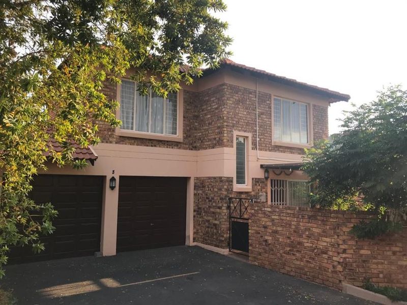 A double-storey face brick home featuring a double garage, paved driveway, and secure boundary wall entrance.