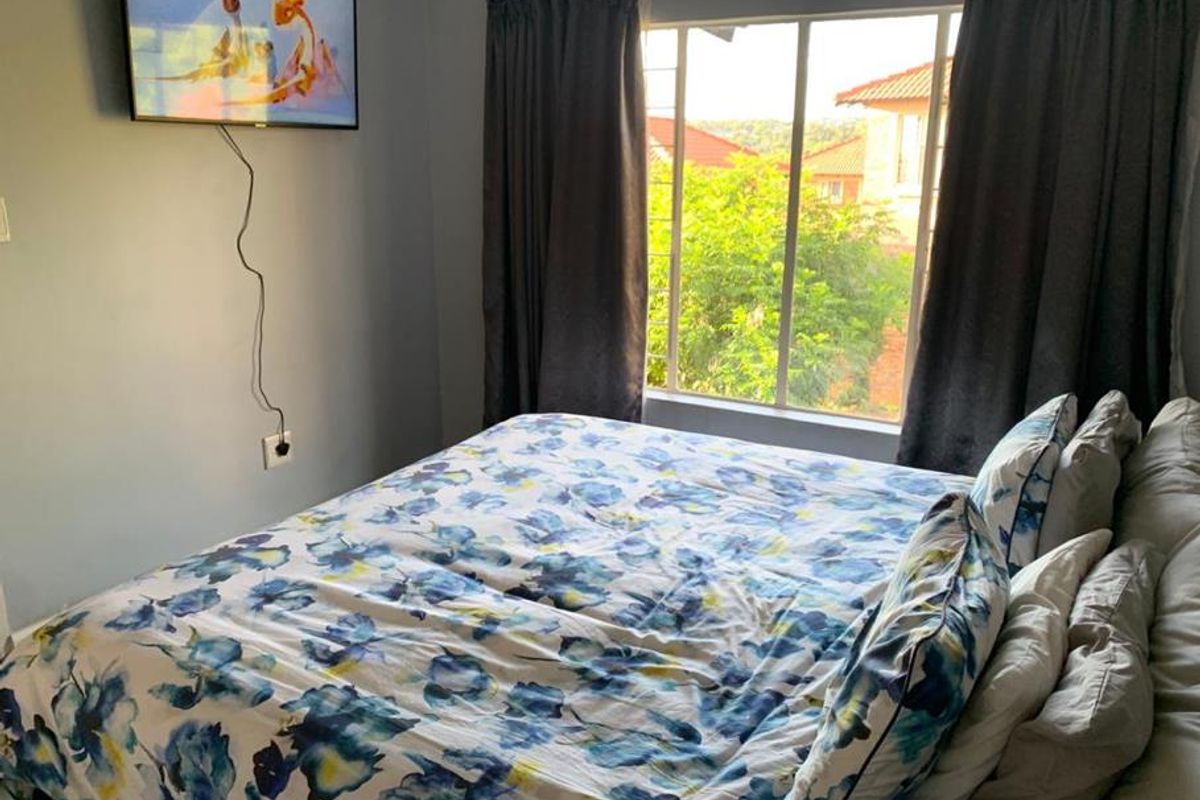A cozy bedroom featuring a large window with natural light and a wall-mounted television setup.