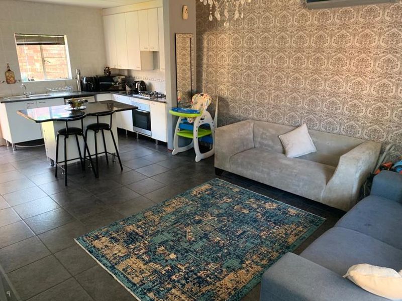 Open-plan living area featuring a modern kitchen with island, tiled flooring, and a feature wallpaper wall, creating a functional and connected living space.