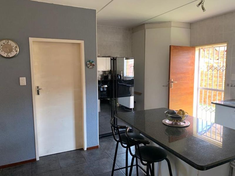 A functional kitchen area featuring a granite-topped breakfast bar, tiled flooring, and direct access to the exterior through a secure door.