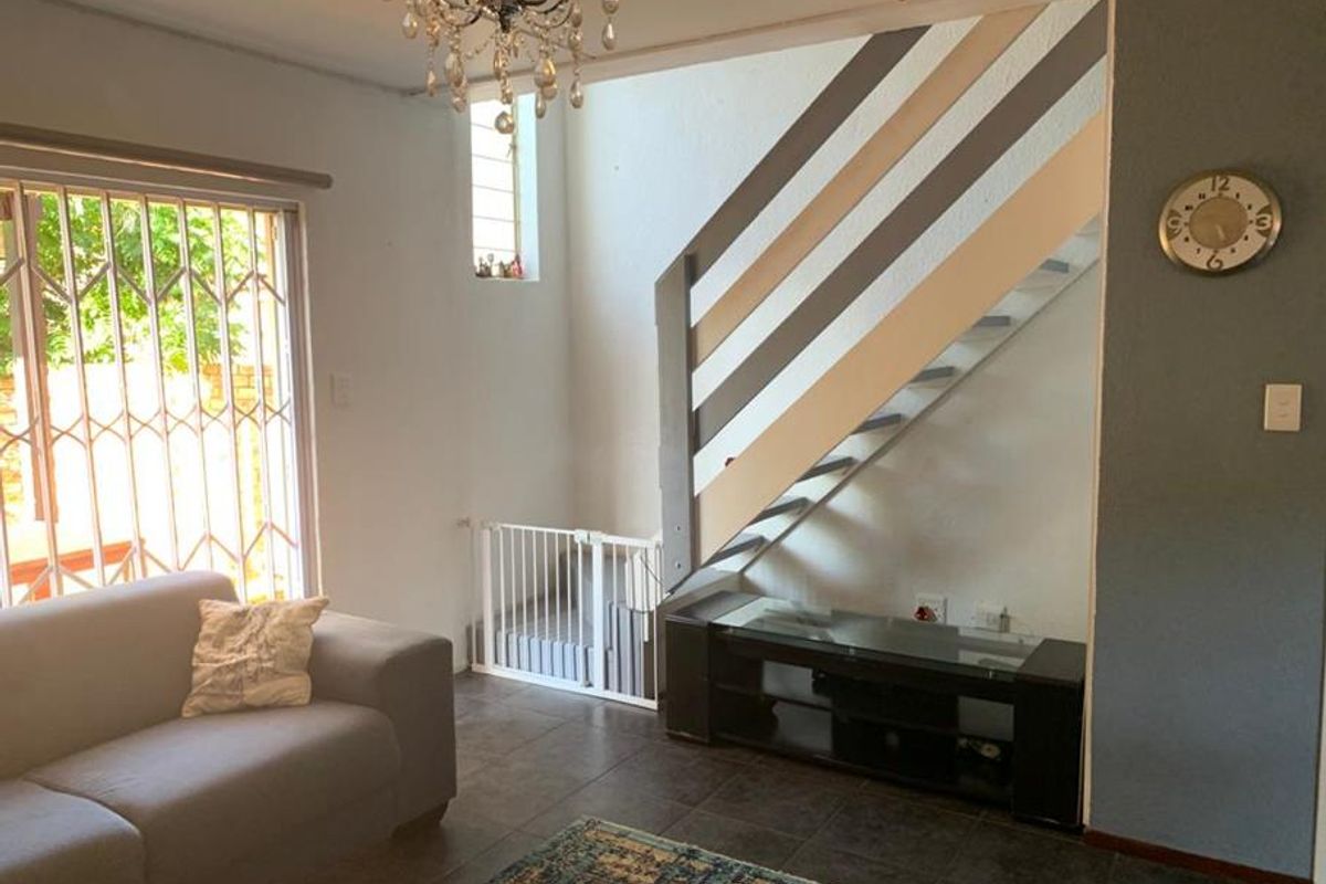 A living room featuring tiled flooring, a staircase with a safety gate, and a sliding door with security bars leading to the exterior.