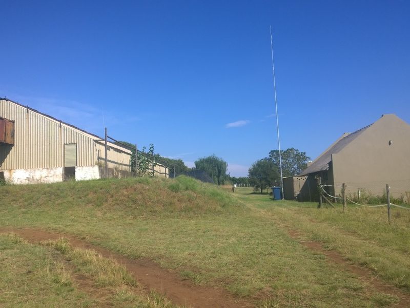View of farm outbuildings including a corrugated metal shed with industrial ventilation and a separate plastered structure on a rural property.