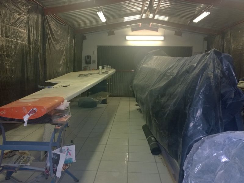 A large utility or workshop space featuring tiled flooring, exposed steel roof trusses, and fluorescent lighting, currently used for storage and project work.