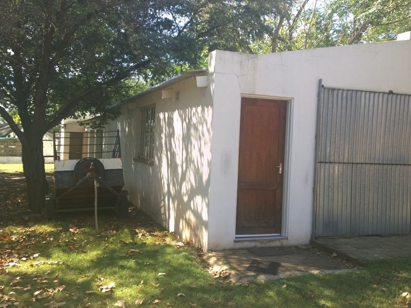 Rear exterior view of a farm outbuilding featuring a corrugated metal garage door, timber entrance door, and plastered masonry walls set in a garden area.