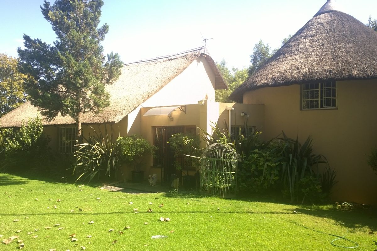Rear view of a traditional farm-style dwelling featuring a thatched roof, plastered walls, and established garden surroundings.