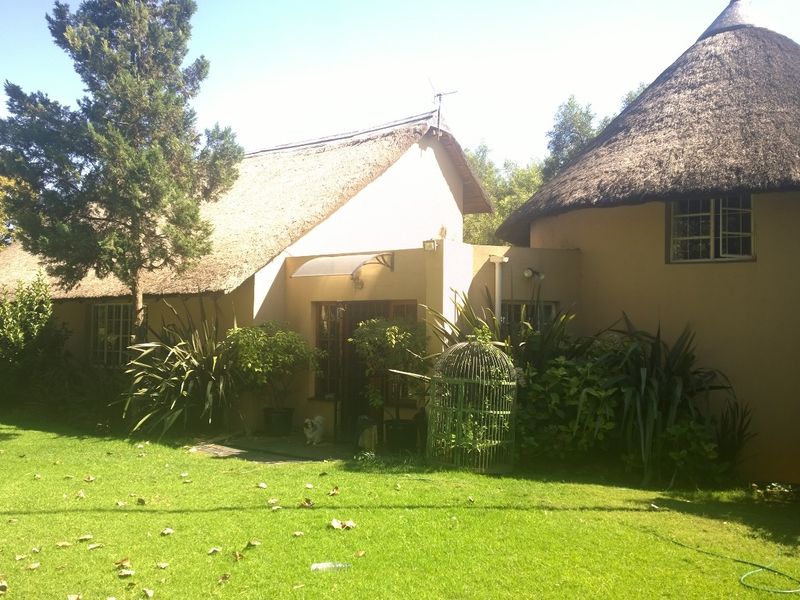 Rear view of a traditional farm-style dwelling featuring a thatched roof, plastered walls, and established garden surroundings.