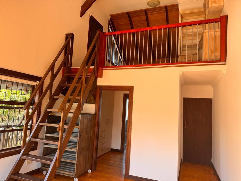 Spacious living area featuring a wooden staircase leading to a mezzanine level, timber ceiling accents, and polished wooden flooring throughout.